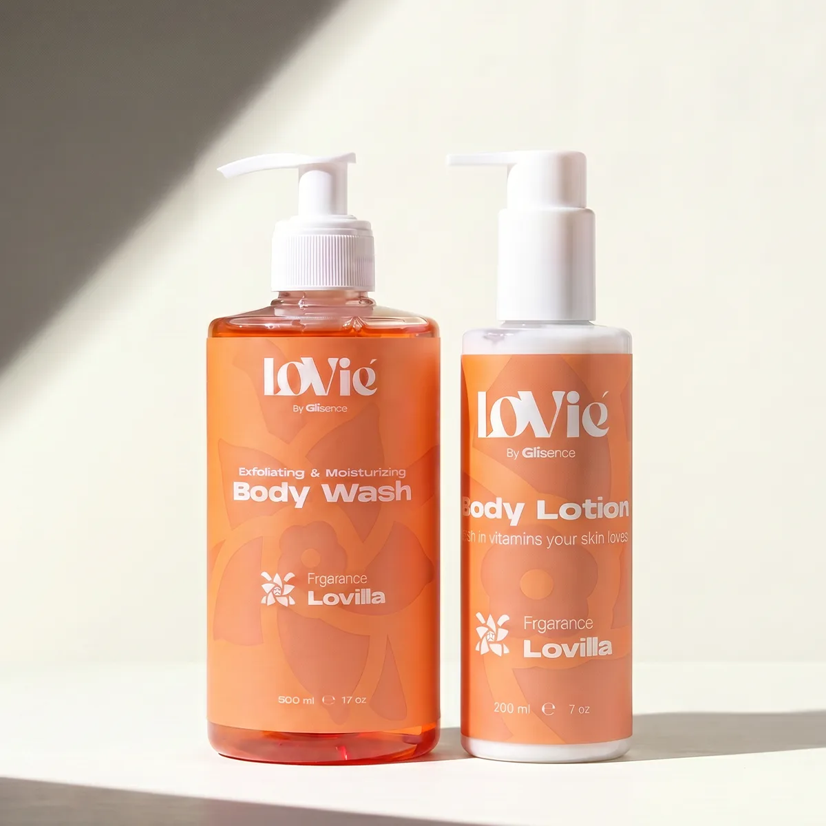 The orange Lovilla body wash and body lotion standing together on a warm seamless background.
