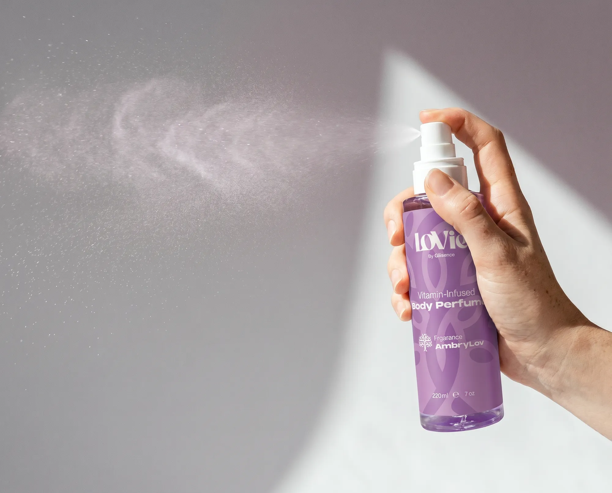 Hand spraying Lovie body perfume, the mist caught mid-air against a hard shadow.