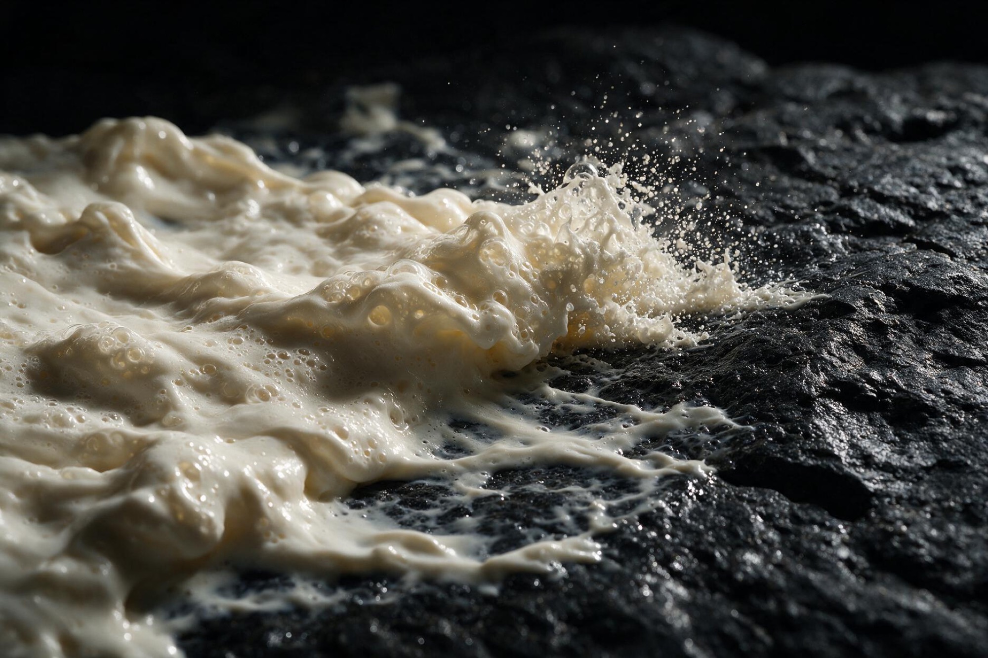 Extreme macro of a cream wave over dark stone under a single hard light.