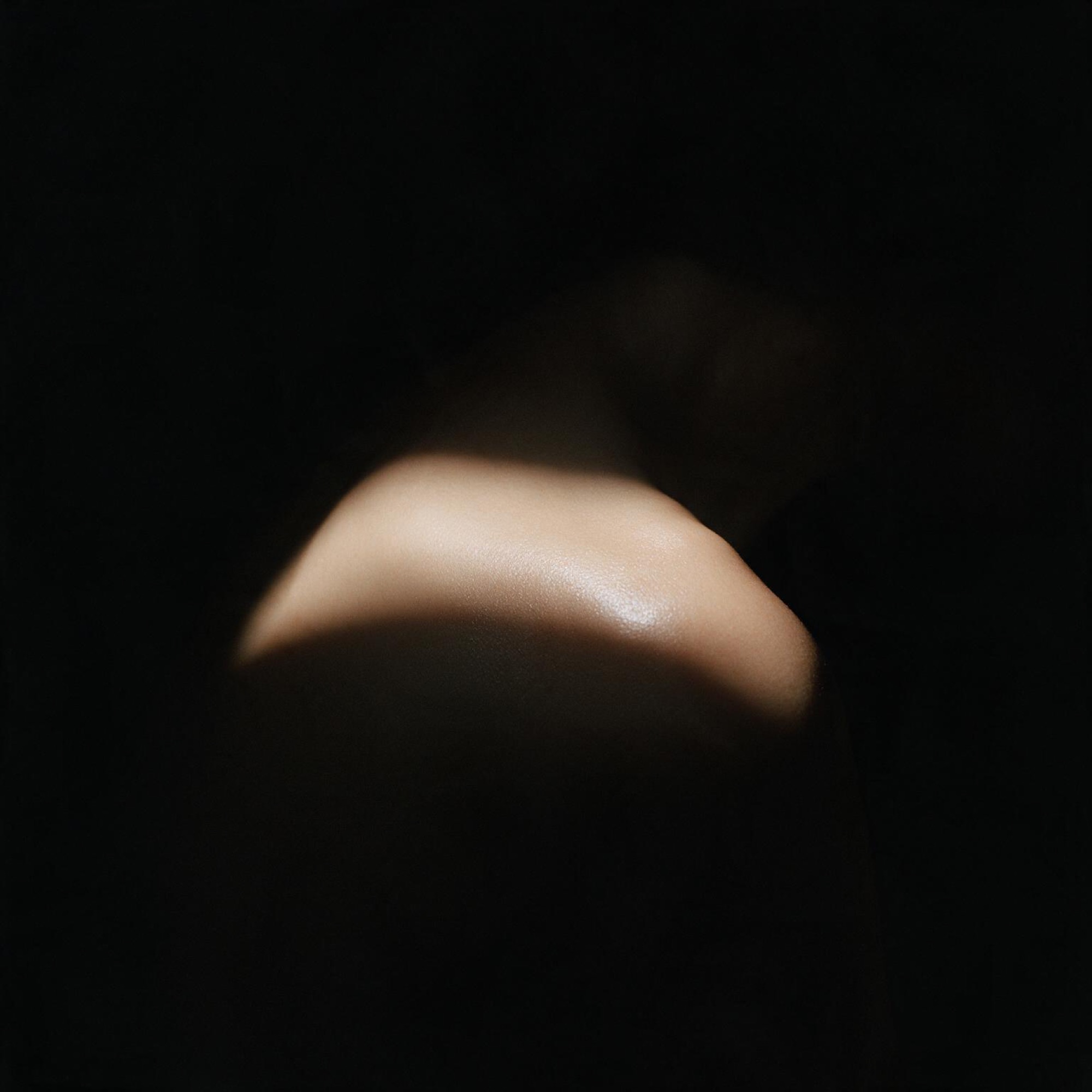 Shoulder and neck emerging from darkness under a narrow strip of light.