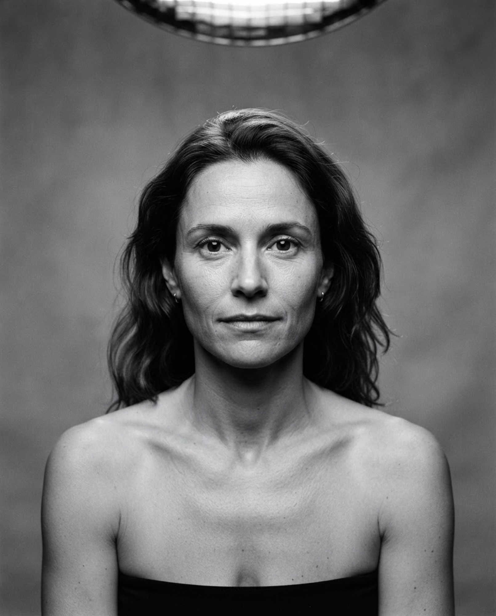 Editorial portrait of a woman with a direct gaze under hard beauty light.