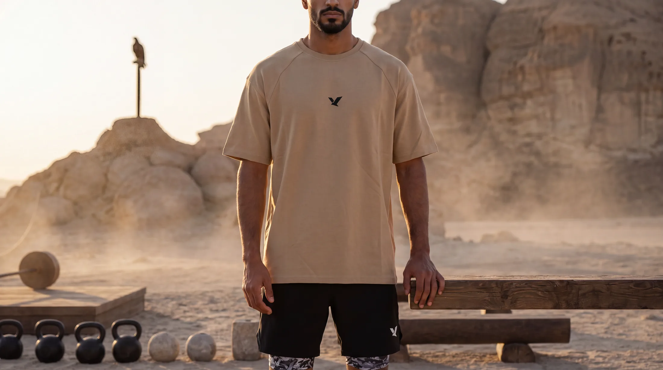 The athlete in a sand-coloured oversized OQAB tee standing at his training ground in warm early light.